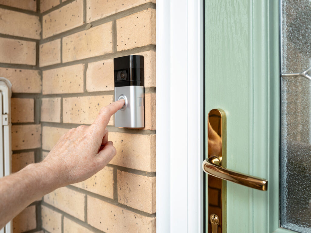 Person pressing doorbell on a smart doorbell outside front door
