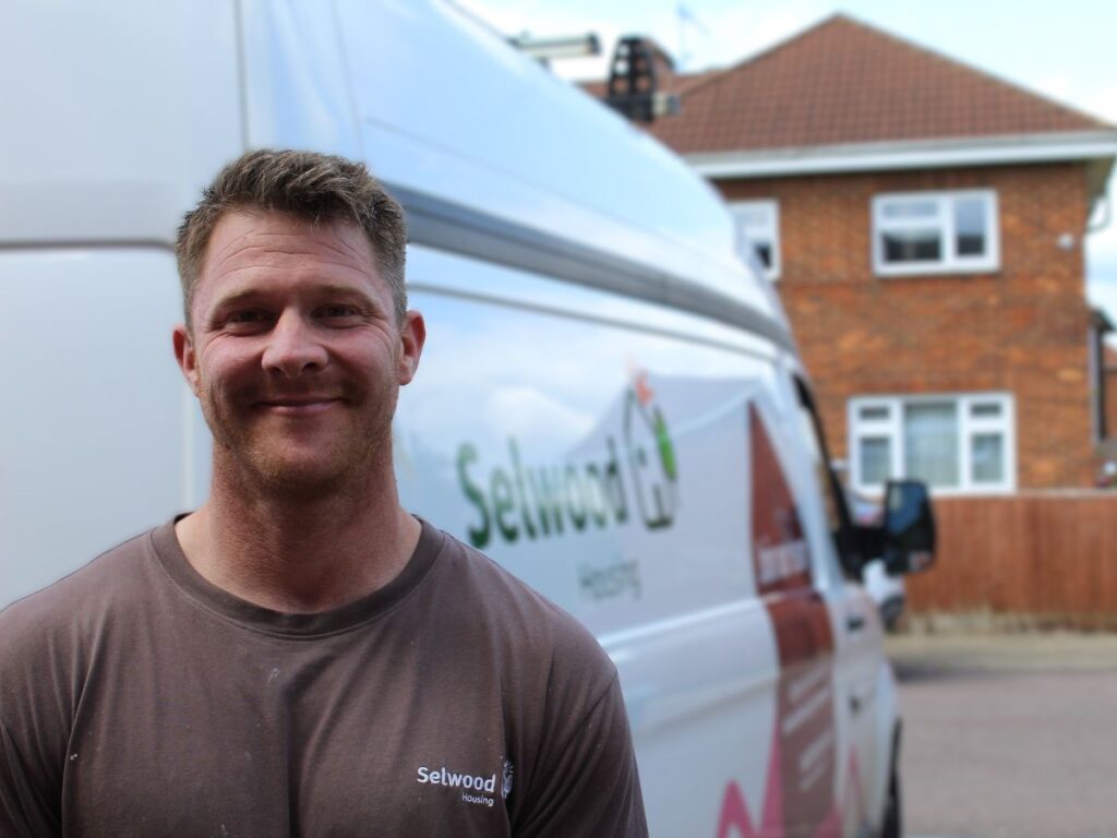 Luke Mead, one of Selwood Housing's multi-skilled plumbers, standing beside a Selwood Housing van near a house.