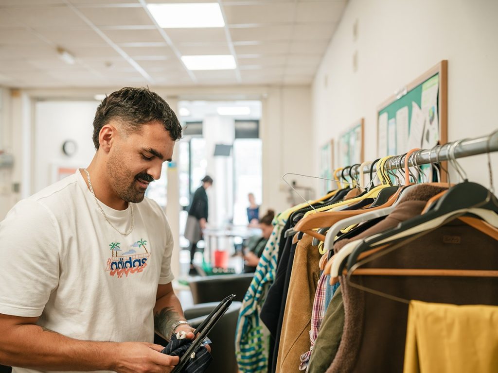 Young man working in a shop hanging clothes on a rail