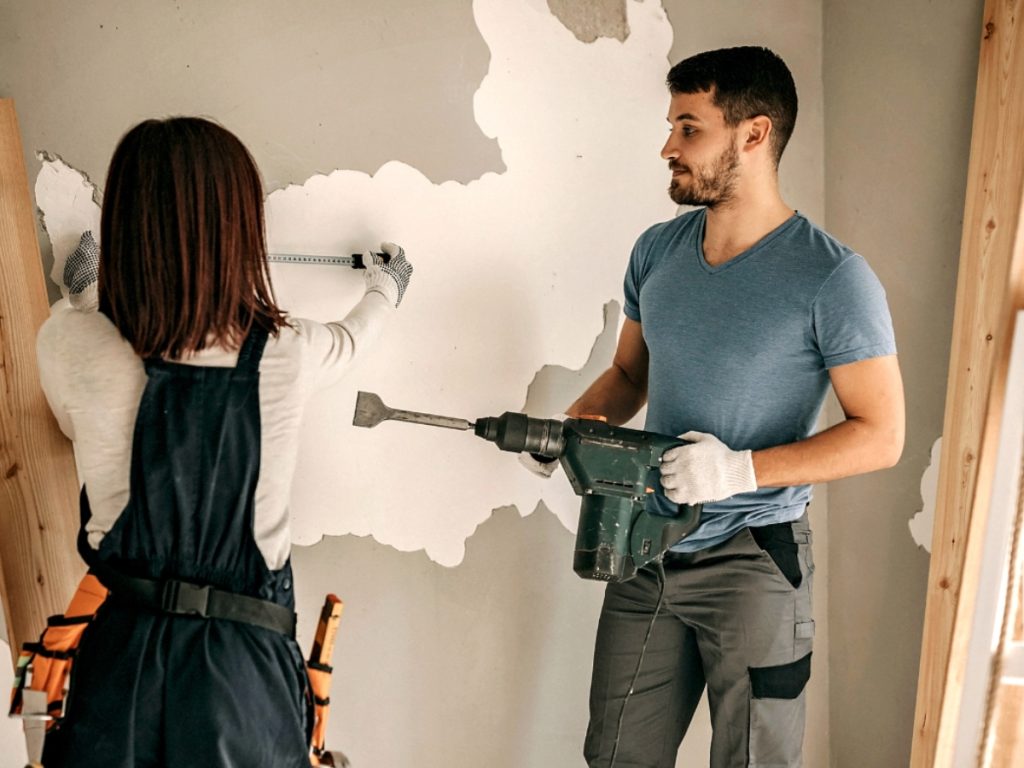 Young couple renovating home taking paint off the wall