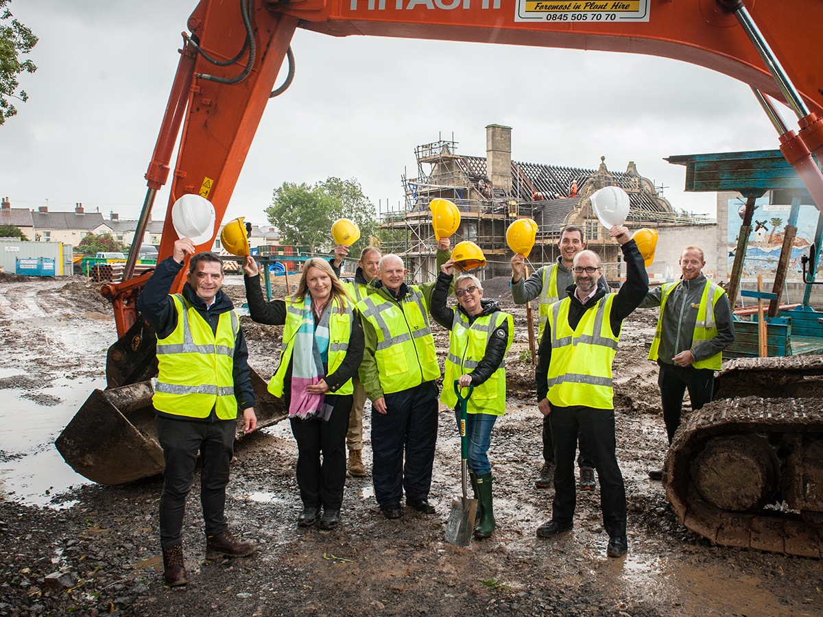 Selwood Housing staff stand at building site in high vis lifting up hard hats