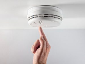 Person pushing button to test fire alarm in the ceiling