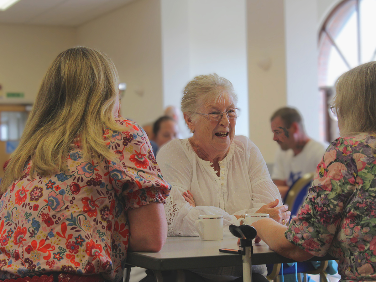 Three women sat round a table talking and laughing