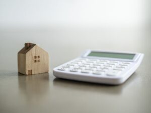 Wooden house figurine beside a calculator