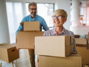 Two happy people carrying boxes inside their new home